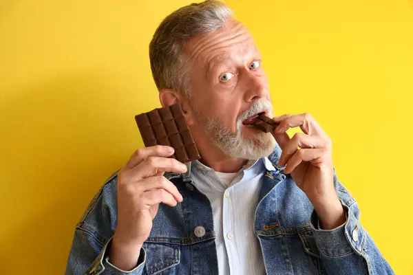 Mature Man Eating Tasty Chocolate Yellow Background Closeup — Stock Photo, Image