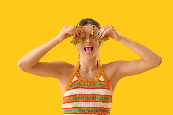 Mujer Joven Con Sabrosos Sándwiches Mostrando Lengua Sobre Fondo Amarillo — Foto de Stock