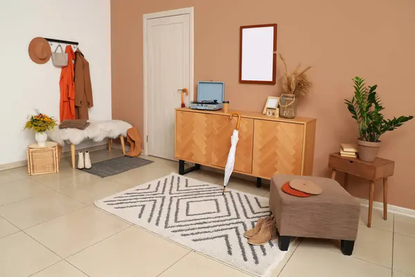 Modern koridorun içinde şık sonbahar kıyafetleri, sedir ve ahşap büfe var.