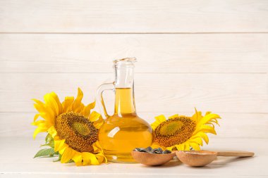 Beyaz ahşap arka planda tohumları olan ayçiçeği yağı ve kaşıklar.