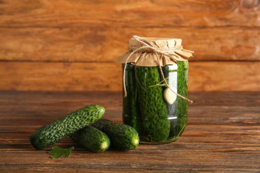 Konserve salatalıklı kavanoz ve ahşap arka planda taze sebzeler.