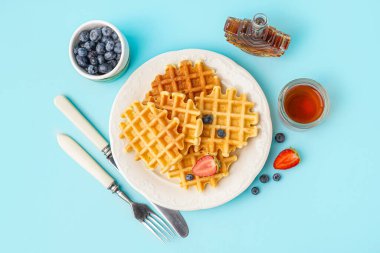 Böğürtlenli lezzetli waffle tabağı ve mavi arka planda akçaağaç şurubu.