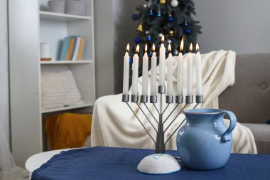 Oturma odasındaki masada Hannukah için süslenmiş sürahi ve Yahudi şapkalı Menorah.