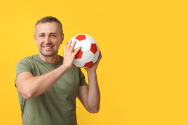 Sarı arka planda futbol topuyla oynayan yakışıklı olgun bir adam.