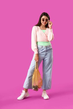 Mor arka planda sicim torbası olan güzel genç bir kadın.