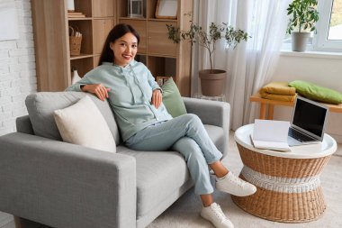 Şık kapüşonlu güzel Asyalı kadın evdeki kanepede oturuyor.