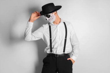 Hafif arka planda boyalı kafatası olan genç bir adam. Meksika Ölüler Günü (El Dia de Muertos) kutlamaları