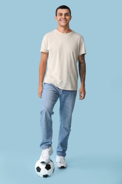 Mavi arka planda futbol topu olan yakışıklı genç adam.