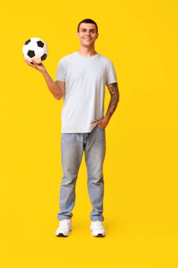 Sarı arka planda futbol topu olan yakışıklı genç adam.