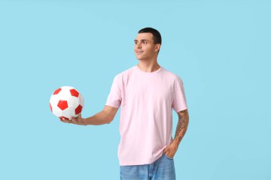 Mavi arka planda futbol topu olan yakışıklı genç adam.