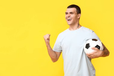 Sarı arka planda futbol topu olan yakışıklı genç adam.