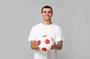 Gri arka planda futbol topu olan yakışıklı genç adam.