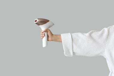 Gri arka planda modern fotoepilatörü olan bornozlu güzel bir kadın.