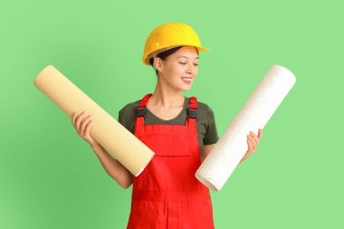 Yeşil arka planda duvar kağıdı ruloları olan Asyalı kadın dekoratör