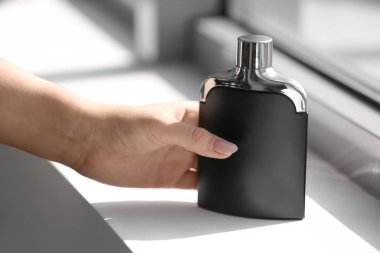 Pencere eşiğinde zarif bir parfüm şişesiyle kadın eli.