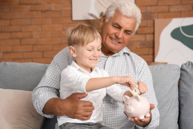 Küçük çocuk ve büyükbabası evdeki domuz kumbarasına para yatırıyor.