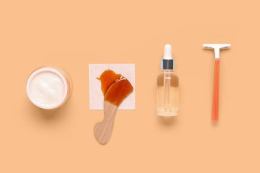 Güvenlik jileti, krema kavanozu, kozmetik yağı ve turuncu arka planda şekerleme macunu.