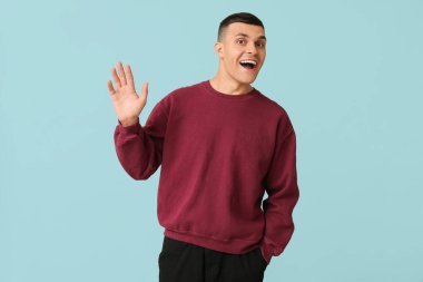 Yakışıklı genç adam mavi arka planda el sallıyor.