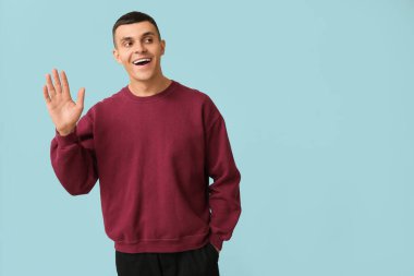 Yakışıklı genç adam mavi arka planda el sallıyor.