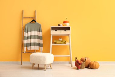 Beyaz masa, balkabağı ve kazak turuncu duvarın yanındaki merdivende asılı.