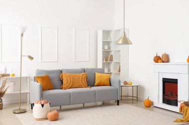 Oturma odasının sonbahar içleri rahat gri kanepe, şömine ve balkabaklarıyla