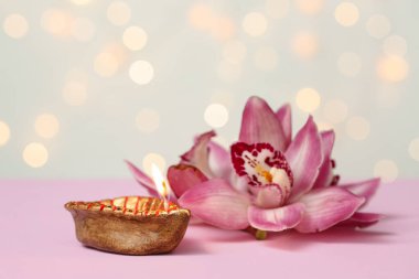 Bulanık ışıklara karşı pembe masanın üzerinde orkide çiçekleri olan Diya lambası. Divaly kutlaması