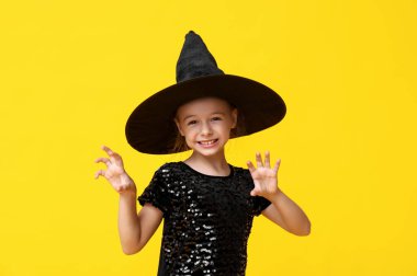 Cadılar Bayramı için sarı arka planda cadı gibi giyinmiş şirin küçük kız.