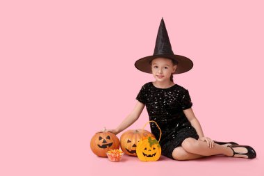 Cadılar Bayramı 'nda çanta, şeker ve balkabaklı cadı gibi giyinmiş şirin küçük kız pembe arka planda oturuyor.