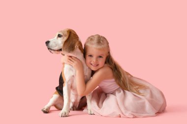 Tatlı küçük kız pembe arka planda Beagle köpeğine sarılıyor.