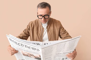 Bej arka planda gazete okuyan olgun gazeteci endişeli