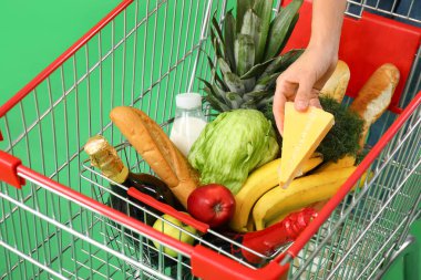 Yeşil arka planda alışveriş arabasına peynir koyan kadın.