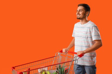 Turuncu arka planda alışveriş arabası olan genç bir adam.