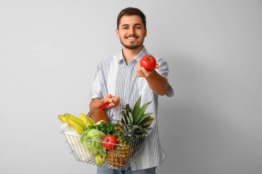 Elinde alışveriş sepeti olan genç bir adam beyaz arka planda taze domates tutuyor.