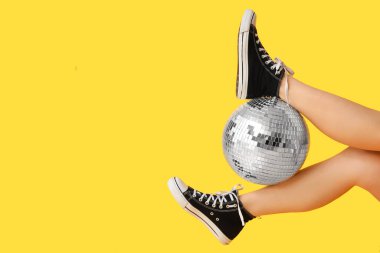 Sarı arka planda disko topu olan kadın bacaklar.