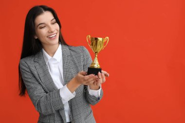 Turuncu arka planda altın kupası olan genç bir iş kadını.