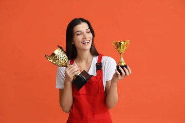 Turuncu arka planda altın bardakları olan kadın işçi.