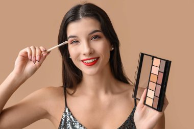 Kahverengi arka planda fırça ve palet sürmüş güzel bir genç kadın.