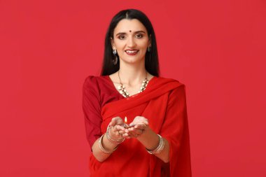 Kırmızı arka planda diya lambası olan sarili güzel bir Hintli kadın. Divaly kutlaması