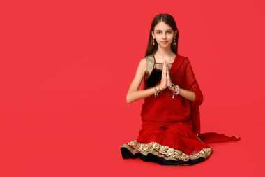 Sari giyip kırmızı arka planda dua eden şirin bir Hintli kız. Divaly kutlaması