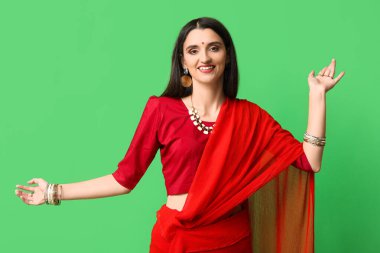 Sari giymiş, yeşil arka planda dans eden güzel bir Hintli kadın. Divaly kutlaması