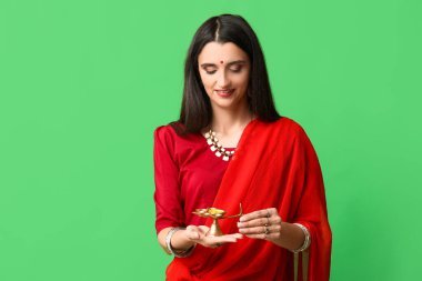 Yeşil arka planda diya lambası olan sarili güzel bir Hintli kadın. Divaly kutlaması