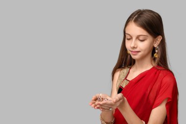 Sari giymiş, gri arka planda diya lambası olan şirin bir Hintli kız. Divaly kutlaması