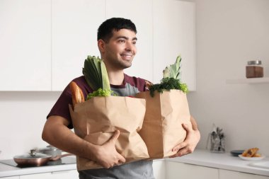 Mutfakta poşetleri olan genç bir adam.
