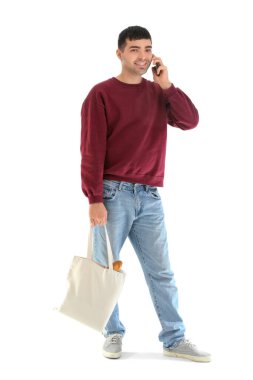 Bakkal çantalı genç adam beyaz arka planda cep telefonuyla konuşuyor.