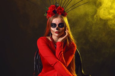 Yüzünde boyalı kafatası ve siyah arka planda renkli dumanı olan genç bir kadın. Meksika Ölüler Günü 'nün Kutlaması (El Dia de Muertos)