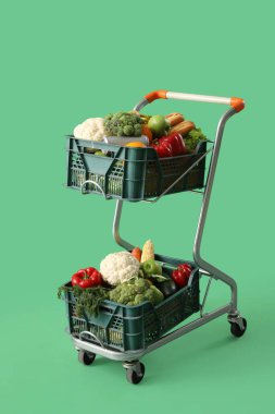 Yeşil arka planda içi taze sebze dolu alışveriş arabası.