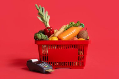 Kırmızı arka planda ödeme terminali ve kredi kartıyla dolu alışveriş sepeti.