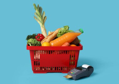 Ödeme terminali ve kredi kartıyla dolu alışveriş sepeti mavi arka planda.