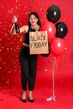Alışveriş çantası, balonlar ve kırmızı arka planda bir şişe şampanyayla güzel bir Afro-Amerikalı kadın. Kara Cuma indirimi