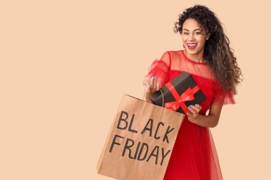 Bej arka planda hediye kutusu ve alışveriş çantası olan güzel bir Afro-Amerikalı kadın. Kara Cuma indirimi